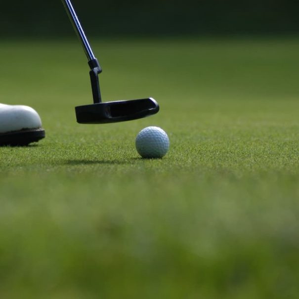 photo of man's shoe with a putter and golf ball