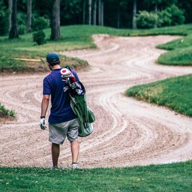 image of a man walking with a golf bag through a sand trap