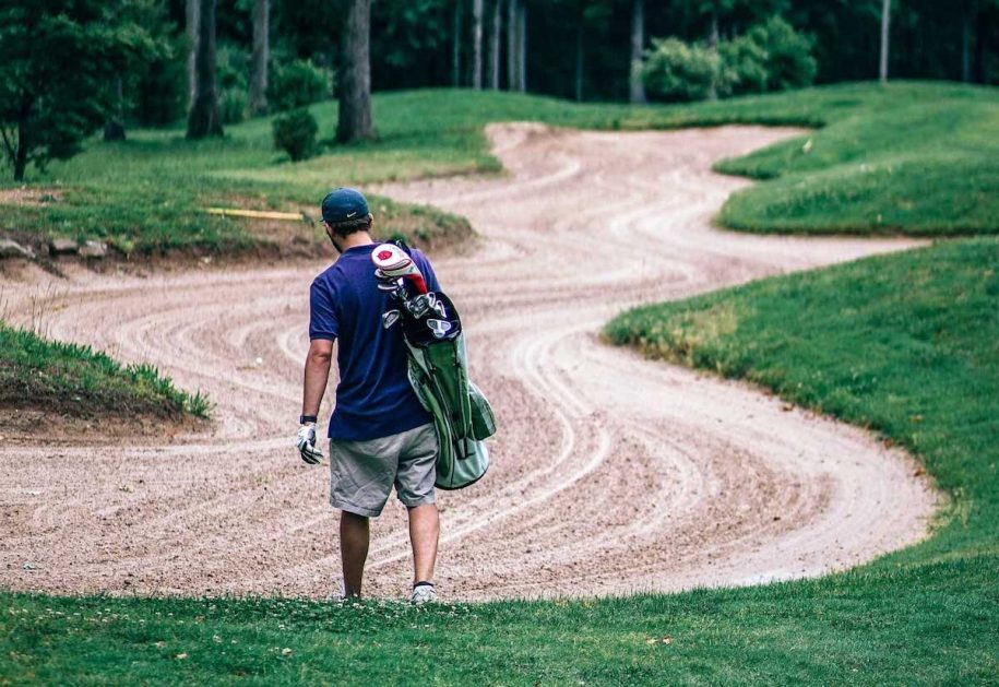 image of a man walking with a golf bag through a sand trap