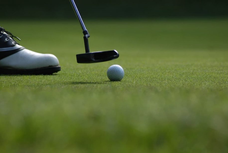 photo of man's shoe with a putter and golf ball